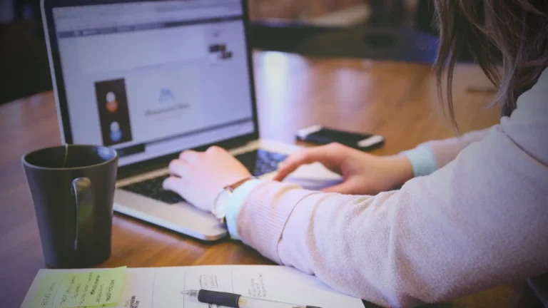 Person working on a laptop with notes and a coffee mug — representing digital product creation and online business planning.
